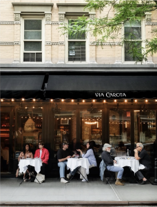 Diners at outdoor café tables under the black Via Carota awning on Grove Street, West Village