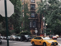 new york yellow taxi driving past a brick townhouse