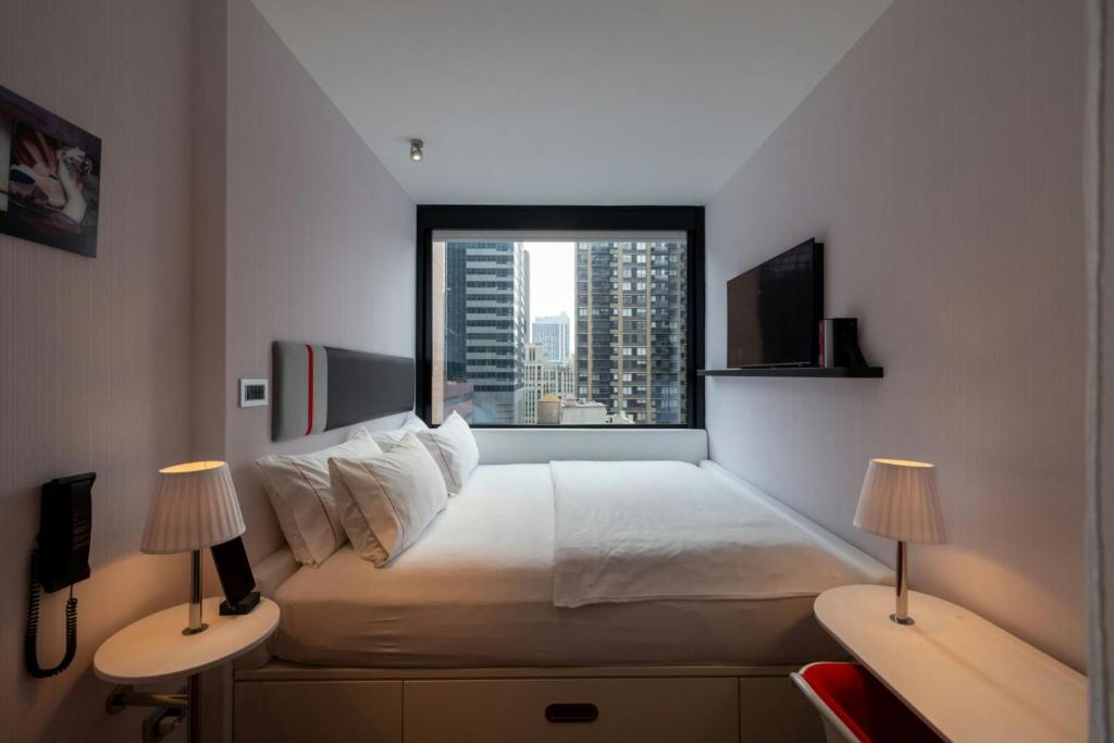 Compact room at citizenM Times Square, with a wall-to-wall king bed beneath a large window overlooking Midtown skyscrapers