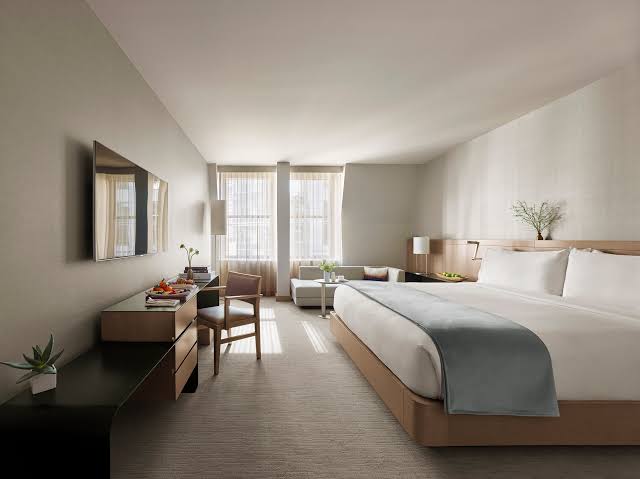 Calm, minimalist bedroom at the Knickerbocker hotel in Times Square, with a king bed, taupe and white decor and tall sunlit windows