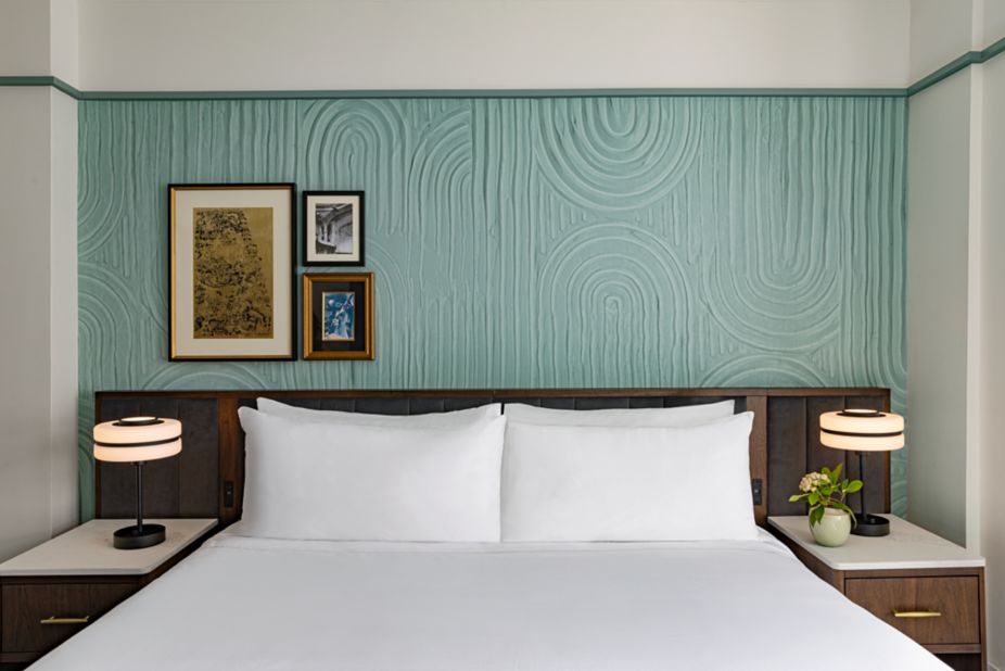 Bedroom at the Algonquin hotel in Midtown Manhattan, with a sculpted sea-green feature wall, framed vintage prints, a king bed and globe bedside lamps